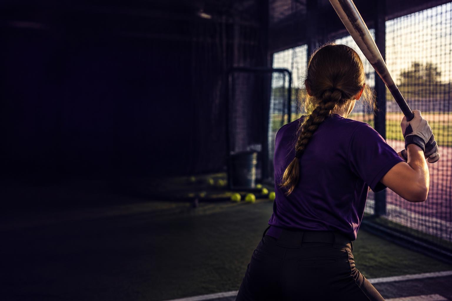 Softball athlete practicing her swing in a batting cage